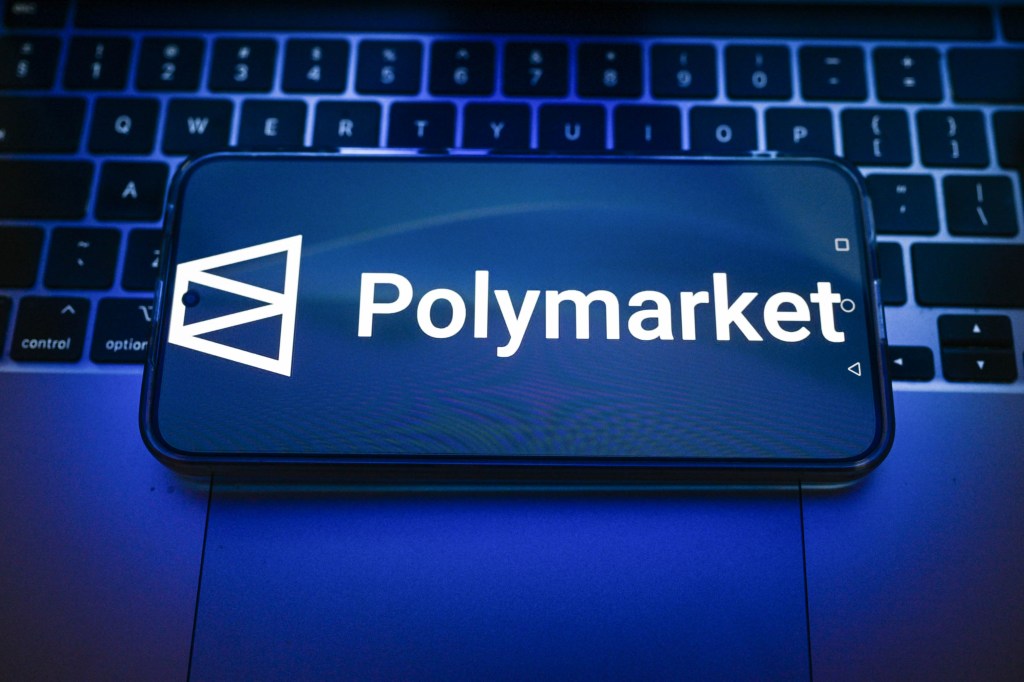 In this photo illustration, a Polymarket logo is displayed on a smartphone on top of a laptop.