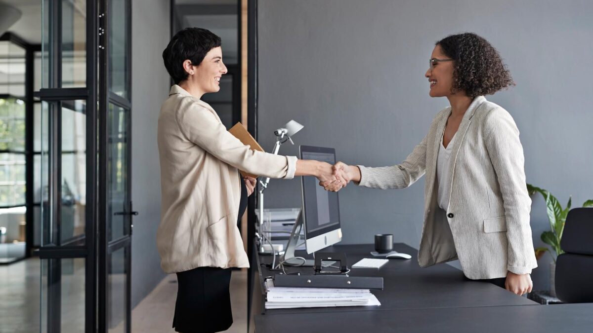 Side view of smiling businesswoman shaking hands with coworker in modern office