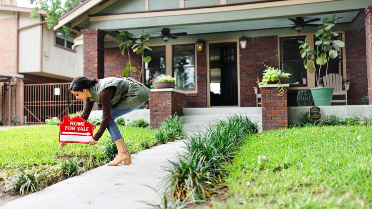 Real estate agent places a For Sale sign in front of a home